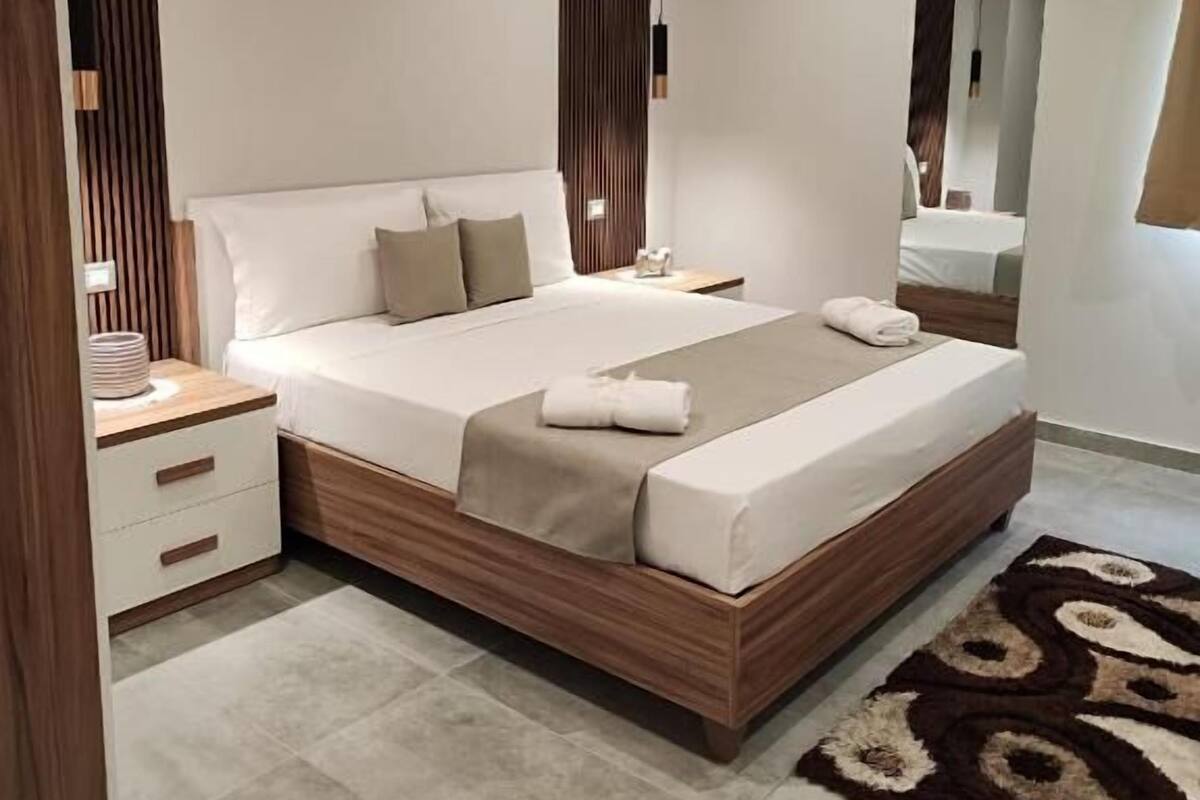 A modern bedroom with a large bed, a nightstand, a mirror, and a patterned rug.