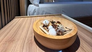 Une chambre d’hôtel avec un lit, un téléviseur fixé au mur et une table en bois sur laquelle se trouve un bol de collations.