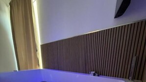 Une salle de bain moderne avec une grande baignoire, un mur recouvert de panneaux en bois et un téléviseur à écran plat fixé au-dessus de la baignoire.