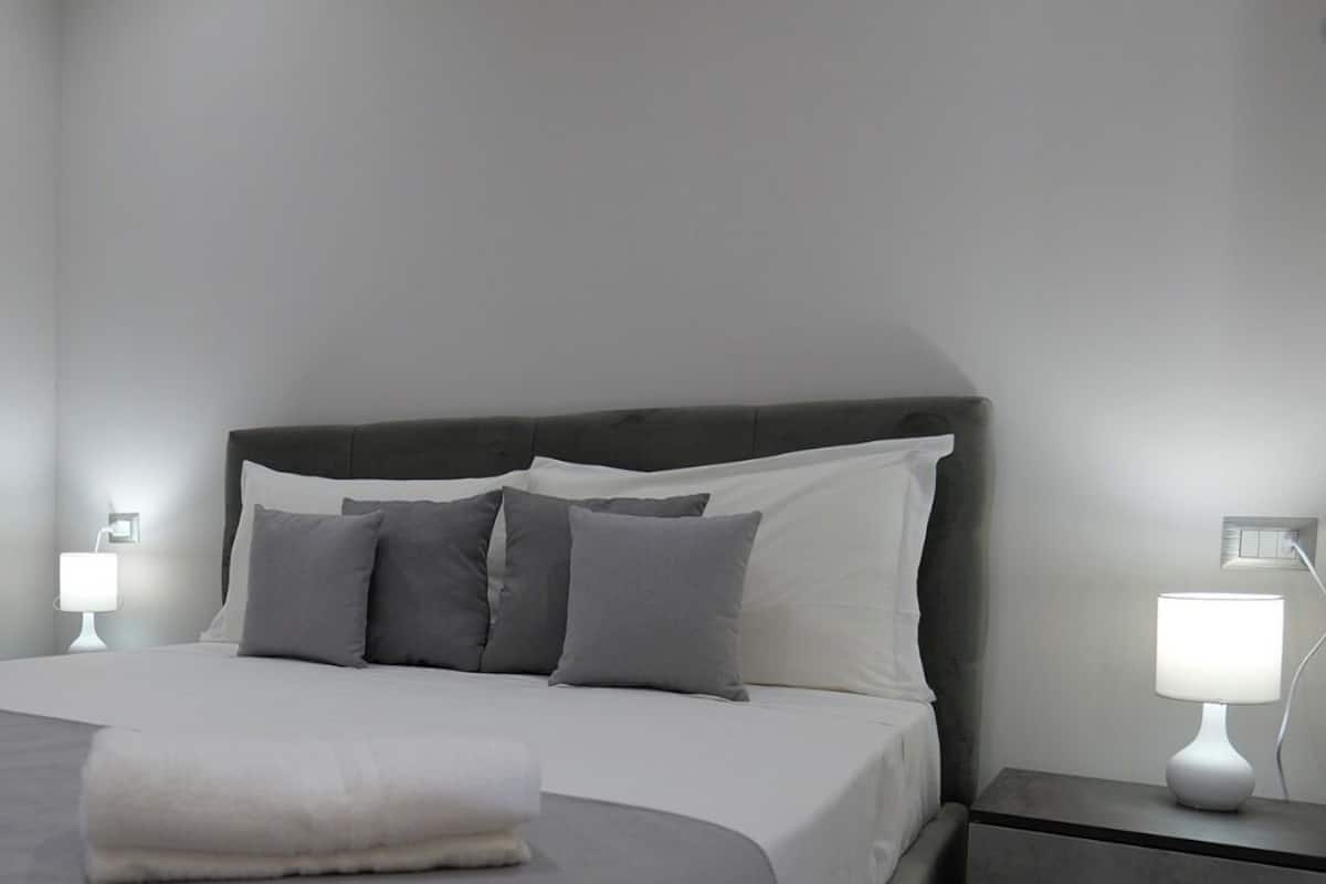 A neatly made bed with pillows and a blanket, two bedside lamps, and a round mirror on the wall.