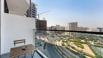 Un balcón con banca de madera y una mesita, con vistas a un paisaje urbano con edificios modernos y una carretera curva.