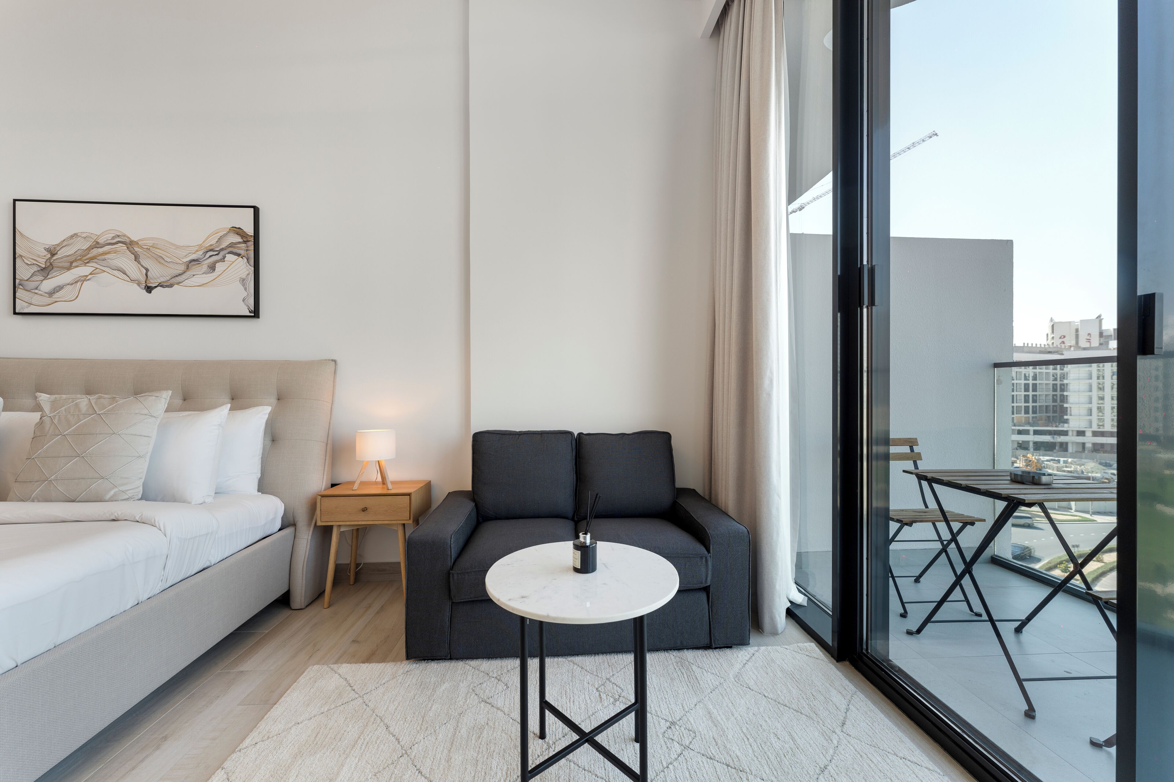 Een moderne hotelkamer met een bed, een bank, een kleine tafel en een balkon met tafel en stoelen.