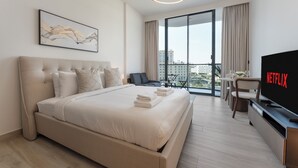 A modern hotel room with a large bed, a flat-screen TV, a dining area with a table and chairs, and a balcony with a city view. - Chic Studio Cinema & Game Room in Arjan (Dubai)