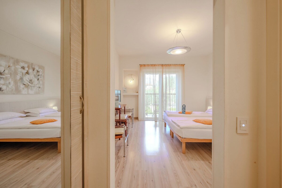 A hotel room with two beds, a desk, a chair, and a large window.