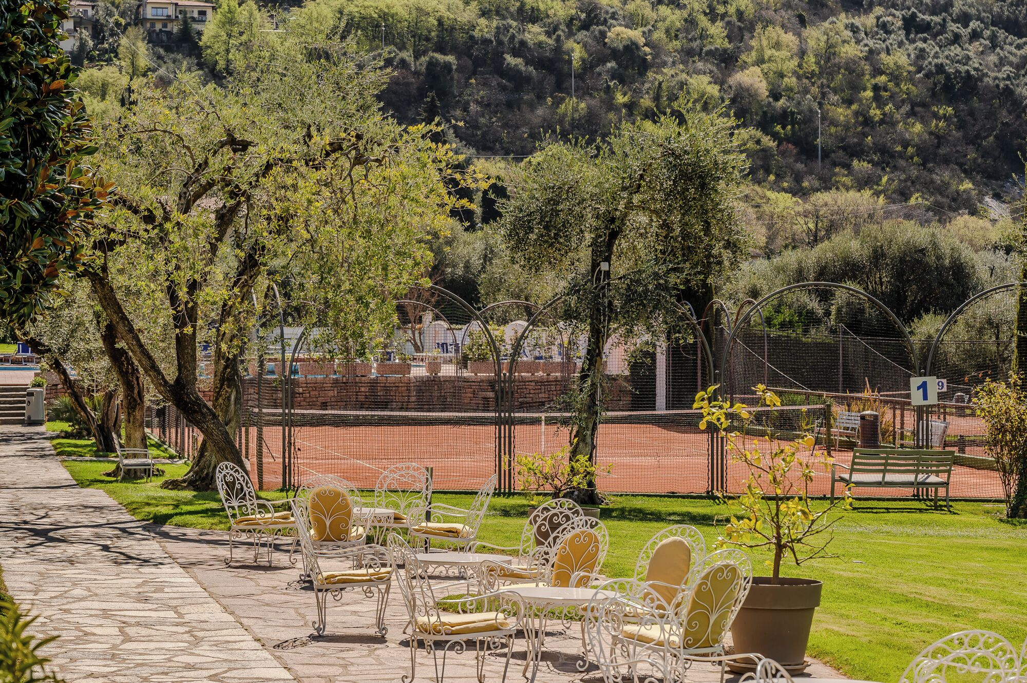 Un patio con mobiliario exterior, cancha de tenis y vistas a una ladera.