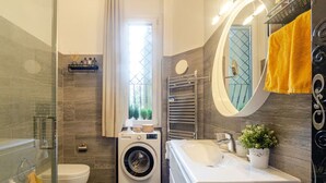 Un baño moderno con ducha de vidrio, lavadora, lavabo y espejo.