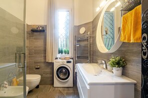 Ein modernes Badezimmer mit Glasdusche, Waschmaschine, Waschbecken und Spiegel.