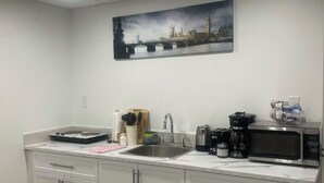 A modern kitchen with white cabinets, a stainless steel sink, a microwave, and a coffee maker. There's a painting of a cityscape on the wall. - A gorgeously cozy 1-bedroom apartment to keep you comfy while you enjoy Regina (Regina)