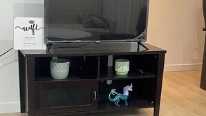 A dark wooden TV stand with a flat-screen TV, a decorative item, and a small cabinet. - A gorgeously cozy 1-bedroom apartment to keep you comfy while you enjoy Regina (Regina)