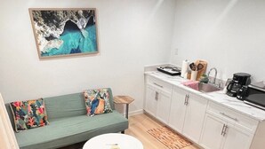 A compact living space with a sofa, a small round table, a kitchen area with cabinets and a countertop, and a painting on the wall. - A gorgeously cozy 1-bedroom apartment to keep you comfy while you enjoy Regina (Regina)