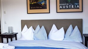 Een hotelkamer met een bed, kussens, een nachtkastje en twee ingelijste posters aan de muur.