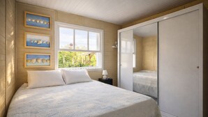 Une chambre à coucher comprenant un lit, une table de chevet, une fenêtre donnant sur un espace verdoyant et une armoire.