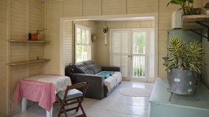Une pièce chaleureuse avec une table à manger, un canapé et un fauteuil. On y trouve des plantes en pot et une grande fenêtre.