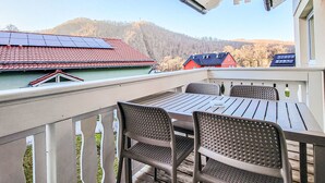A balcony with a table and chairs, overlooking a red-roofed building and a forested hill. - Hotelpark-Bodetal by Interhome (Thale)