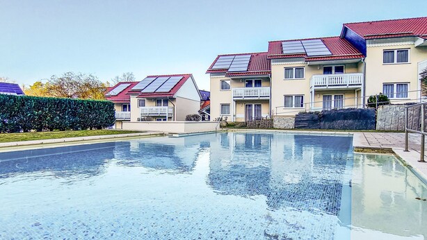 A swimming pool with a tiled floor, surrounded by apartment buildings with red roofs and solar panels. - Hotelpark-Bodetal by Interhome (Thale)