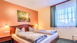 A hotel room with a large bed, two bedside tables, a wall-mounted painting, and a window with curtains. - Hotelpark-Bodetal by Interhome (Thale)