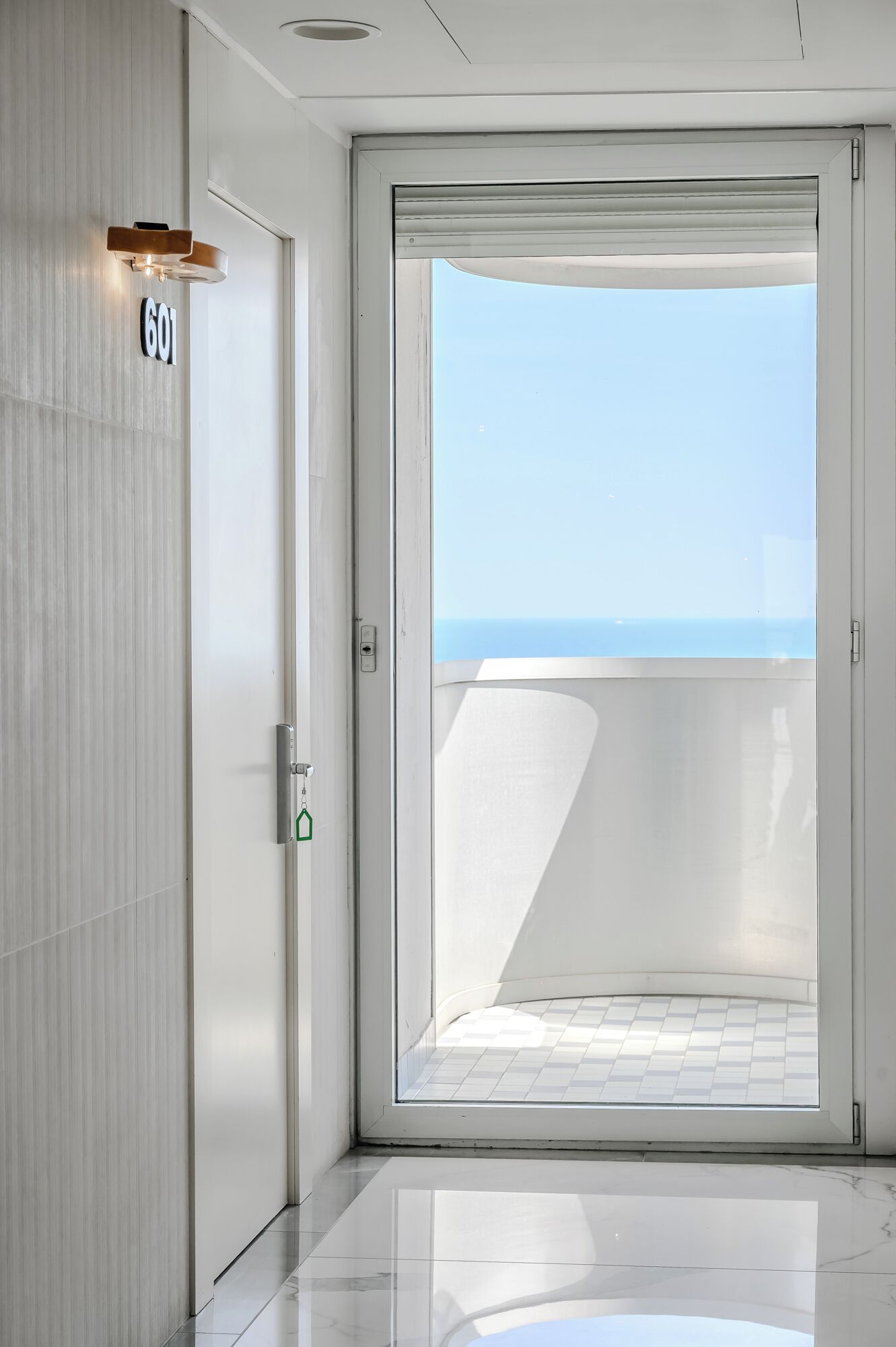 A modern hotel room with a large sliding glass door leading to a balcony with a view of the sea.
