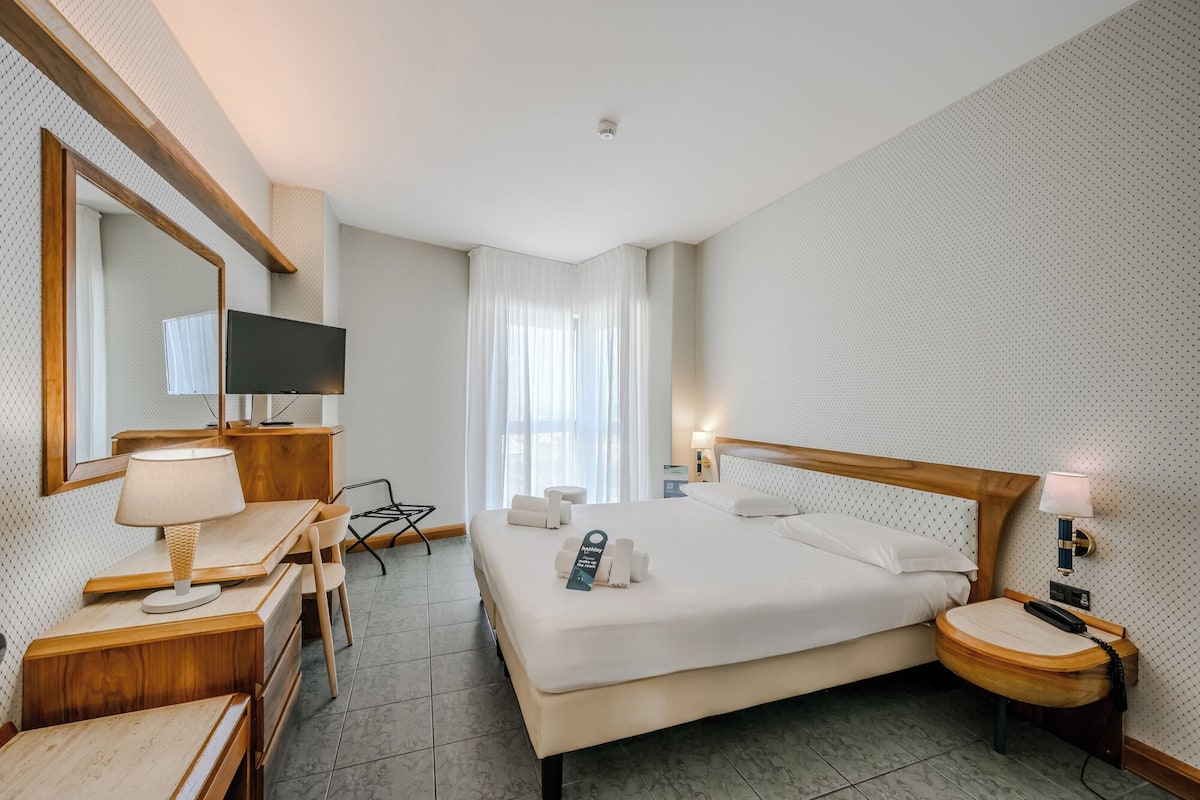 A hotel room with a bed, a desk, a chair, a TV, and a bathroom.