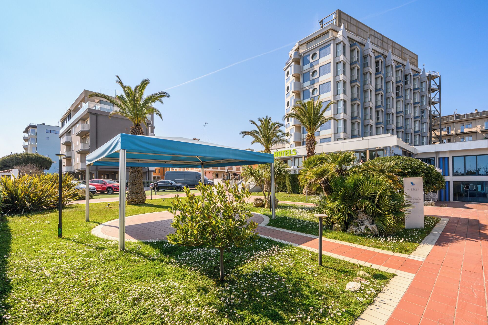 A hotel with a modern design, a covered outdoor seating area, and a well-maintained garden.