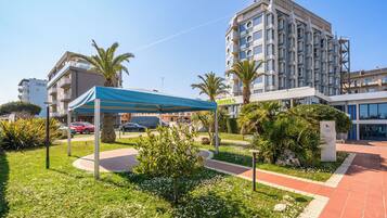 A hotel with a modern design, a covered outdoor seating area, and a well-maintained garden.