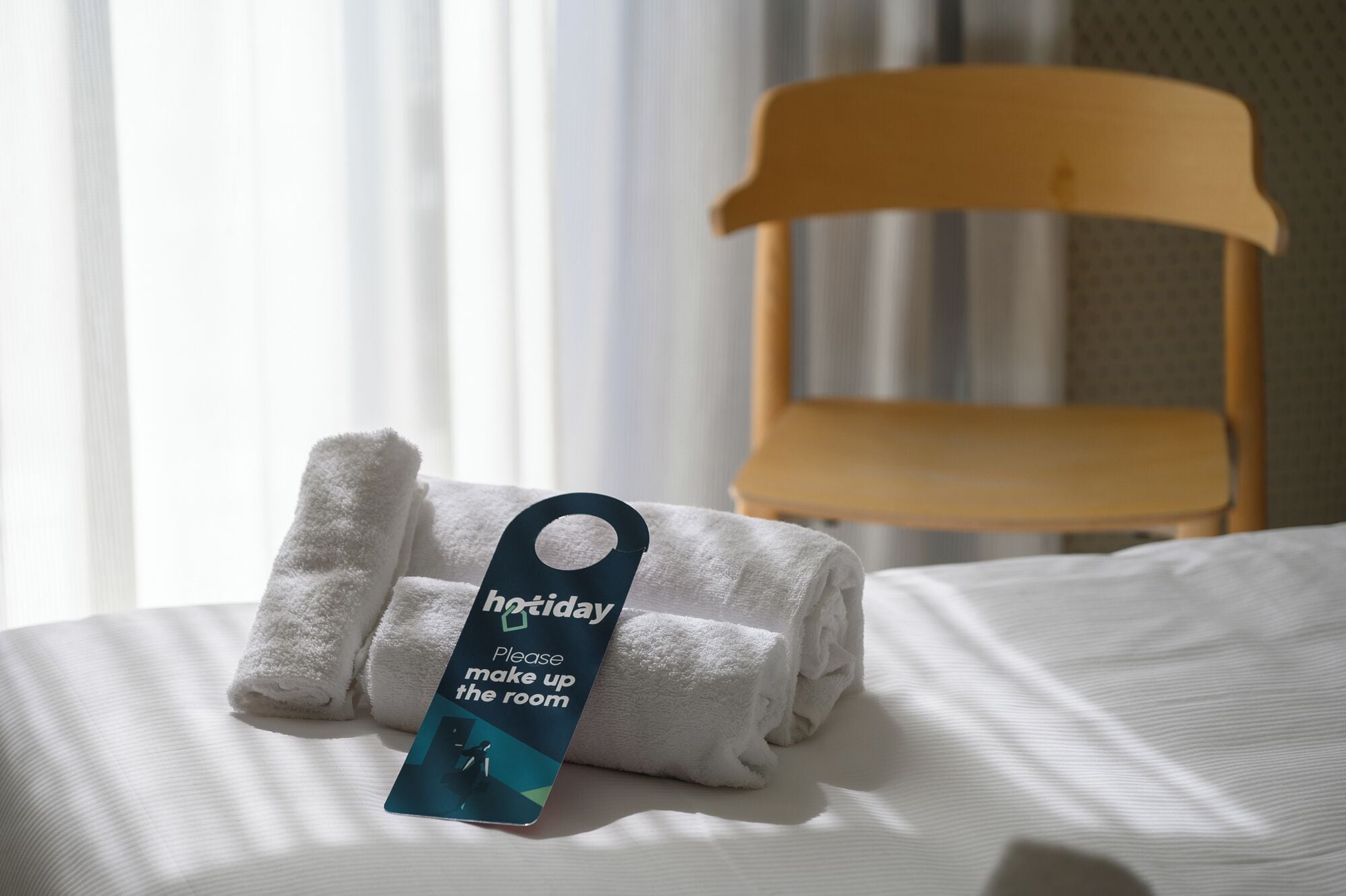 Ein ordentlich bezogenes Bett mit gefalteten weißen Handtüchern und einem Etikett am Bett.