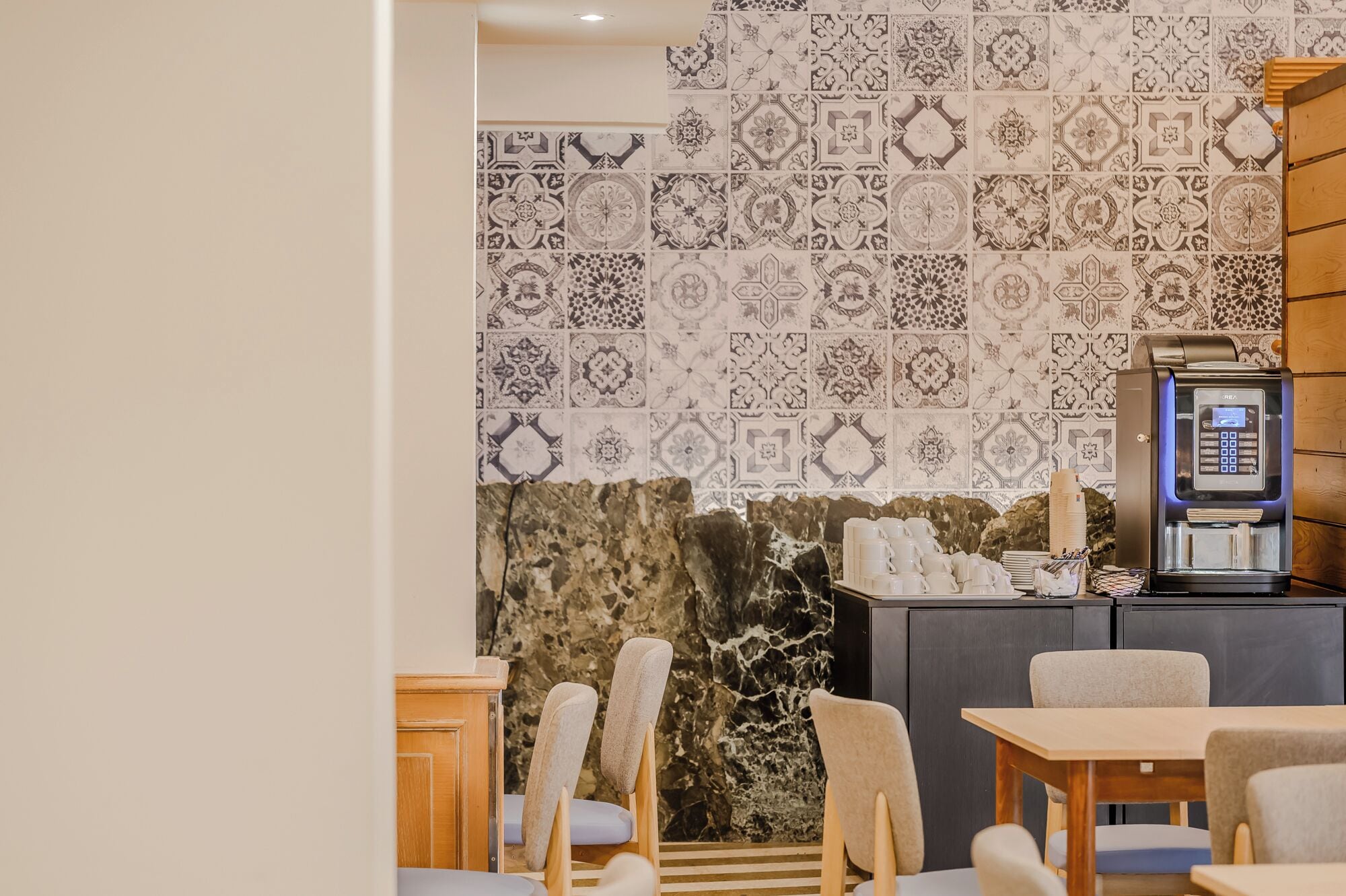 Una habitación de hotel con pared de mármol, máquina de café y zona de estar con sillas y mesa.