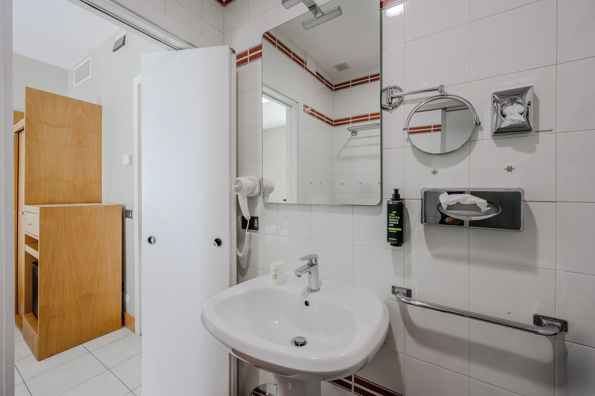 A bathroom with a white sink, a mirror, a towel dispenser, and a hairdryer.