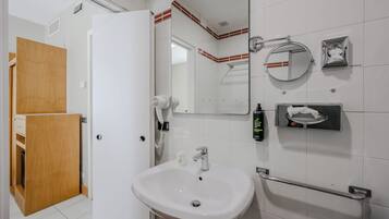 A bathroom with a white sink, a mirror, a towel dispenser, and a hairdryer.