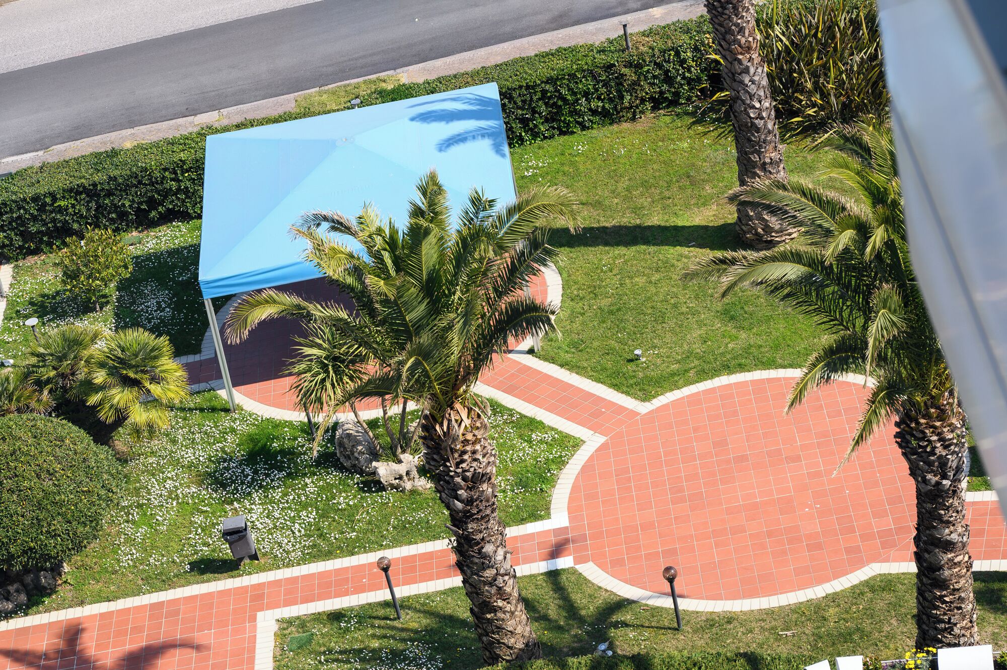 Ein angelegter Garten mit Palmen, einem blauen Bauwerk und einem roten Ziegelweg.