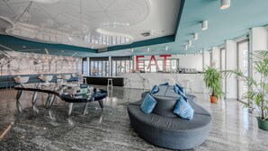 Un lobby moderno con un área de estar curva, un bar y un gran letrero que dice 'EAT'.