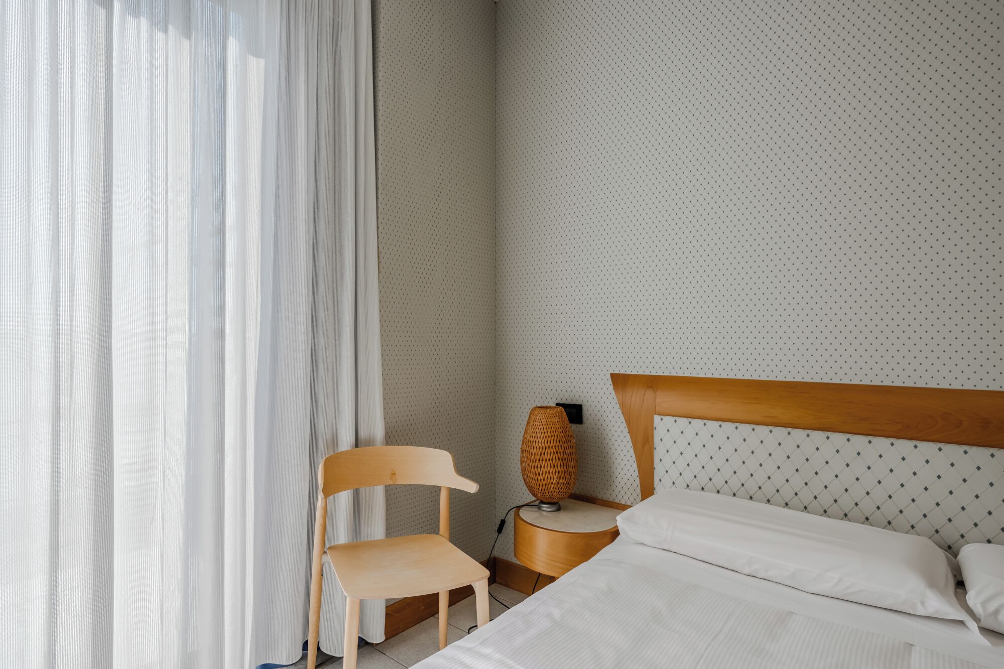 A bedroom with a bed, a chair, a nightstand, and a lamp.