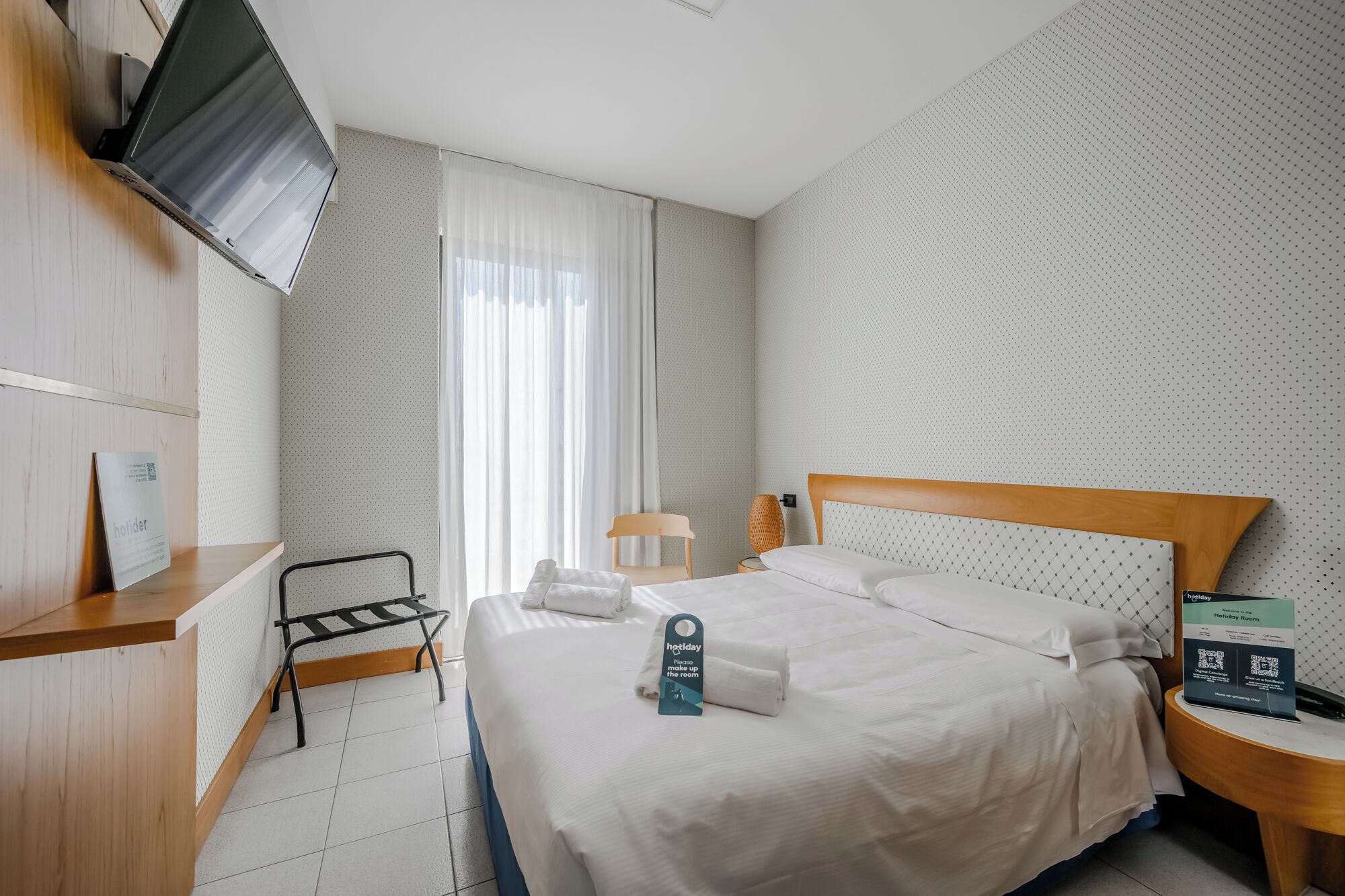 Une chambre d’hôtel équipée d’un lit, d’un bureau, d’une chaise, d’une télévision et d’une fenêtre avec des rideaux.