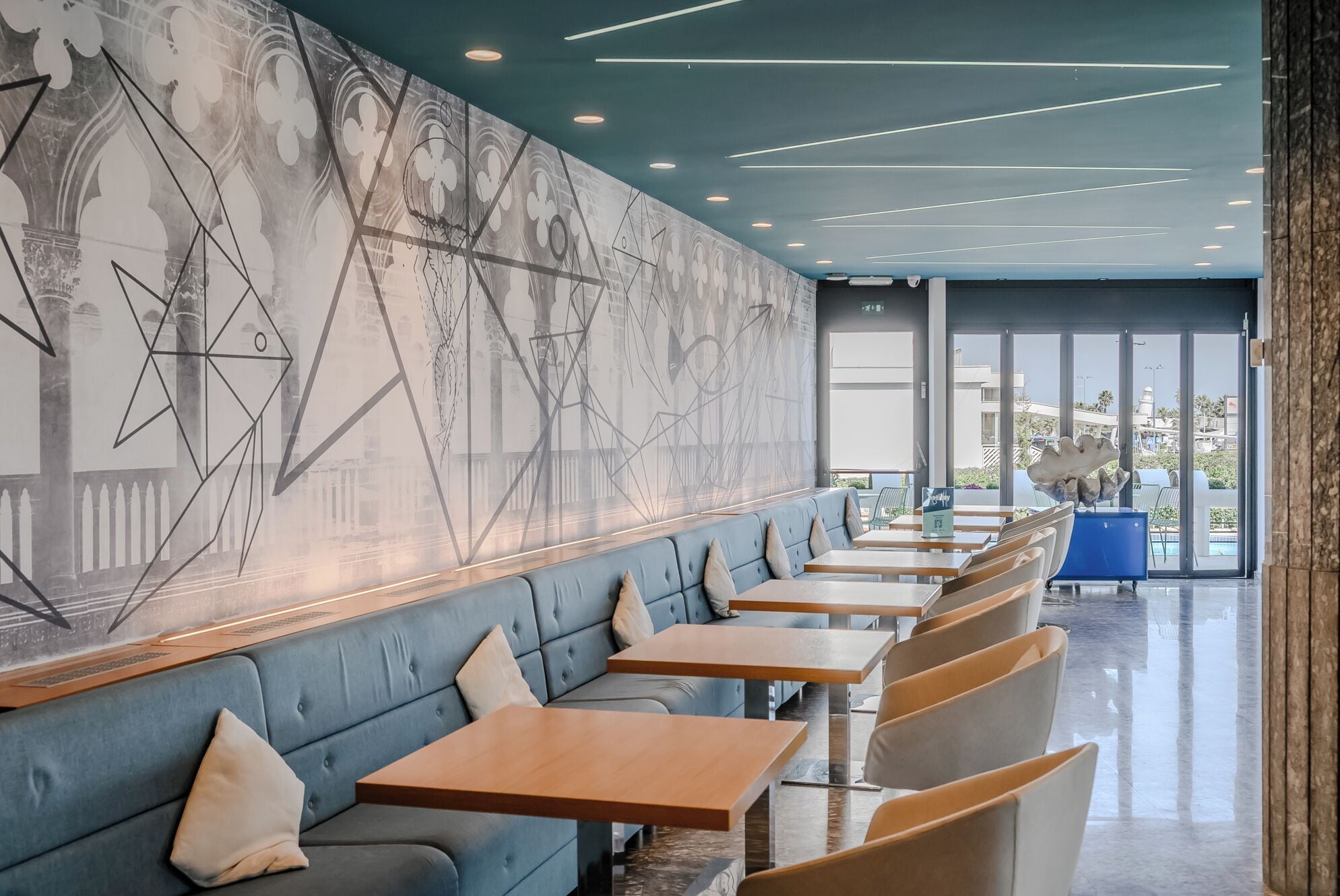 Ein modernes Restaurant mit einer langen Theke, gepolsterten Sitzgelegenheiten und einer großen Wandmalerei.