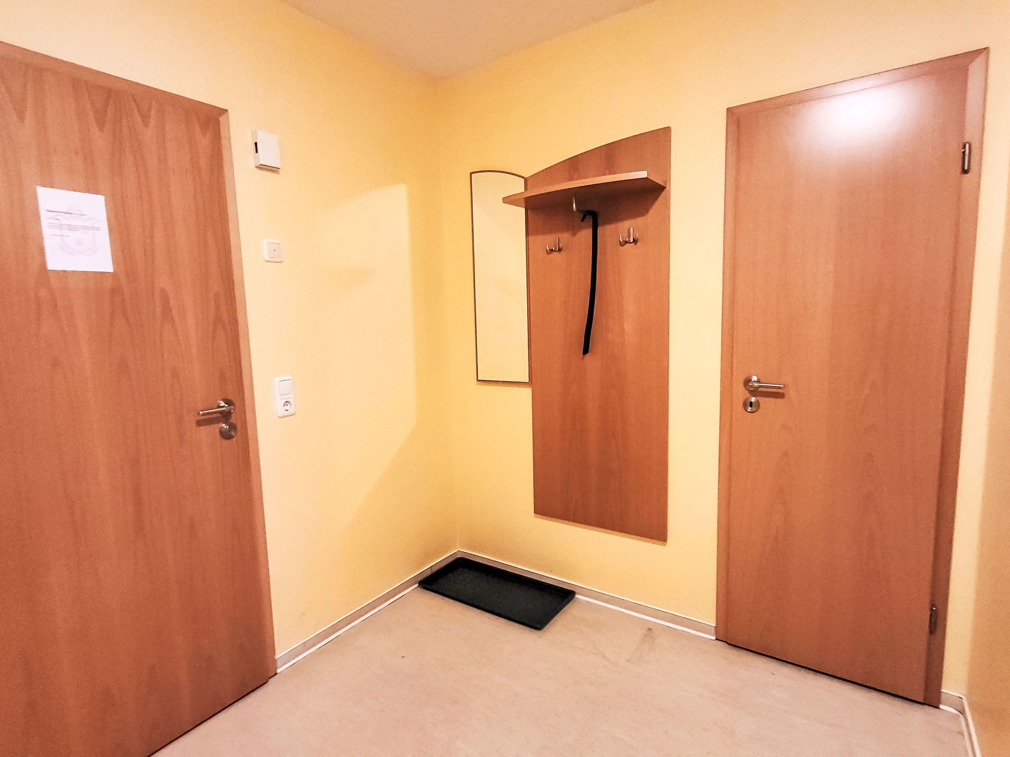 Un passadís amb dues portes de fusta, un petit mirall i un interruptor de llum a la paret.
