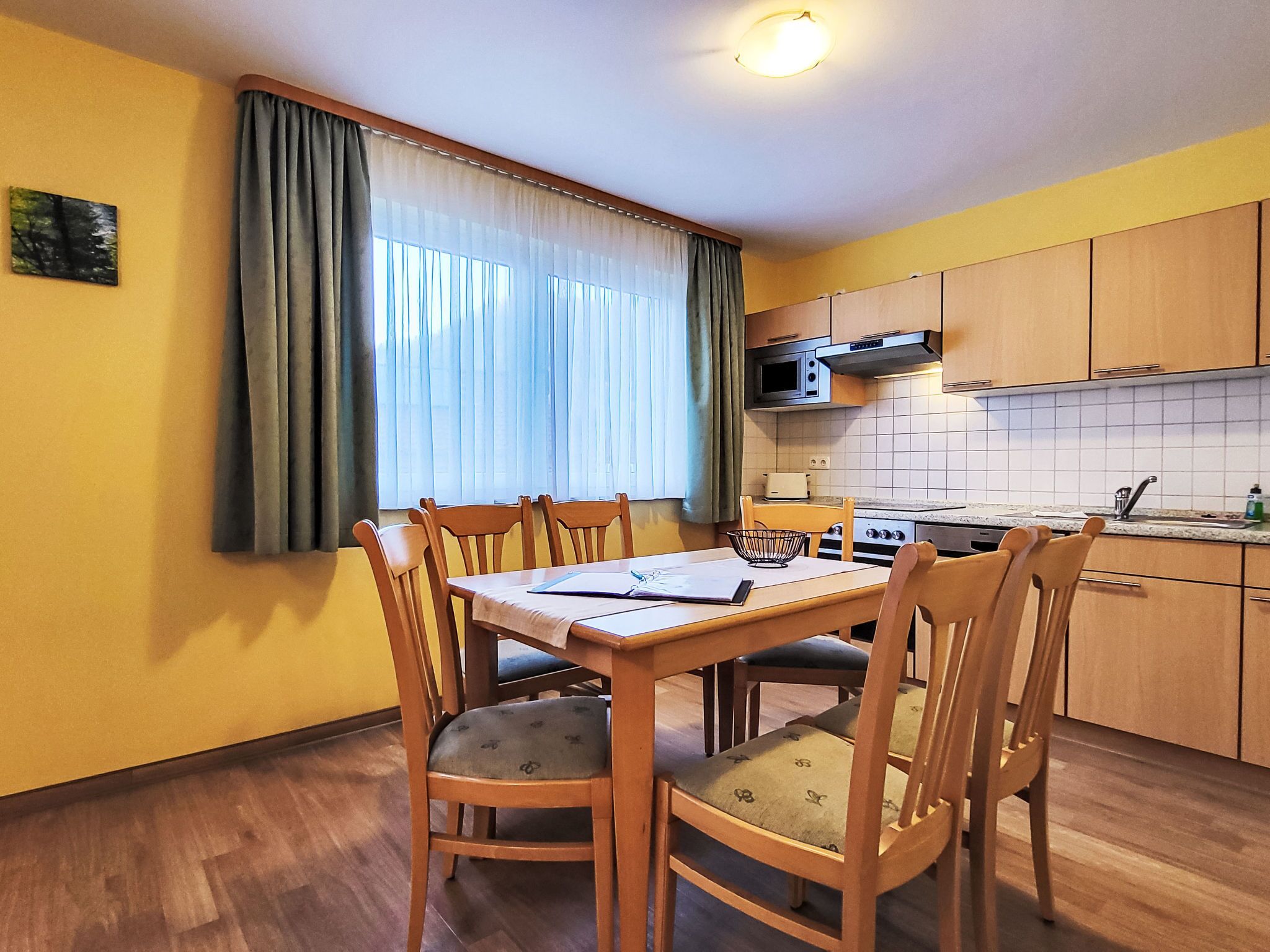 Cocina compacta con armarios de madera, microondas y una mesa de comedor con sillas.