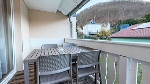 Un balcone con tavolo e sedie, affacciato su una zona residenziale con case e una collina.