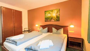 Una camera d'albergo con due letti, un armadio, un quadro e lampade da comodino.