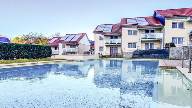 Una piscina con pavimento piastrellato, circondata da edifici residenziali a più piani con balconi e pannelli solari.