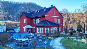 A red building with a balcony, surrounded by outdoor seating and a paved walkway. - Hotelpark-Bodetal by Interhome (Thale)