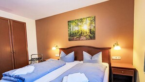 A double bed with blue bedding, two bedside tables with lamps, a wardrobe, and a painting of a forest on the wall. - Hotelpark-Bodetal by Interhome (Thale)