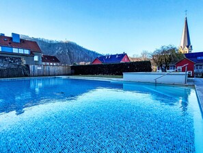 Una piscina amb una superfície d'aigua blava i cristal·lina, envoltada de cases i d'una església amb un campanar alt.