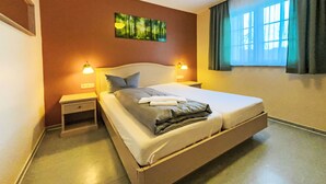 Une chambre d’hôtel avec un grand lit, deux tables de chevet, un tableau au mur et une fenêtre avec des rideaux.