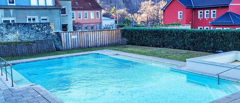 A swimming pool with a stone border, surrounded by a wooden fence and a hedge.