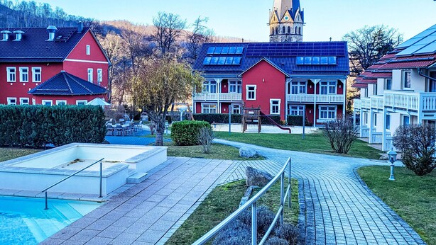Asuinalue, jossa on punaisia ja valkoisia taloja, korkean tornin omaava kirkko ja uima-allas.