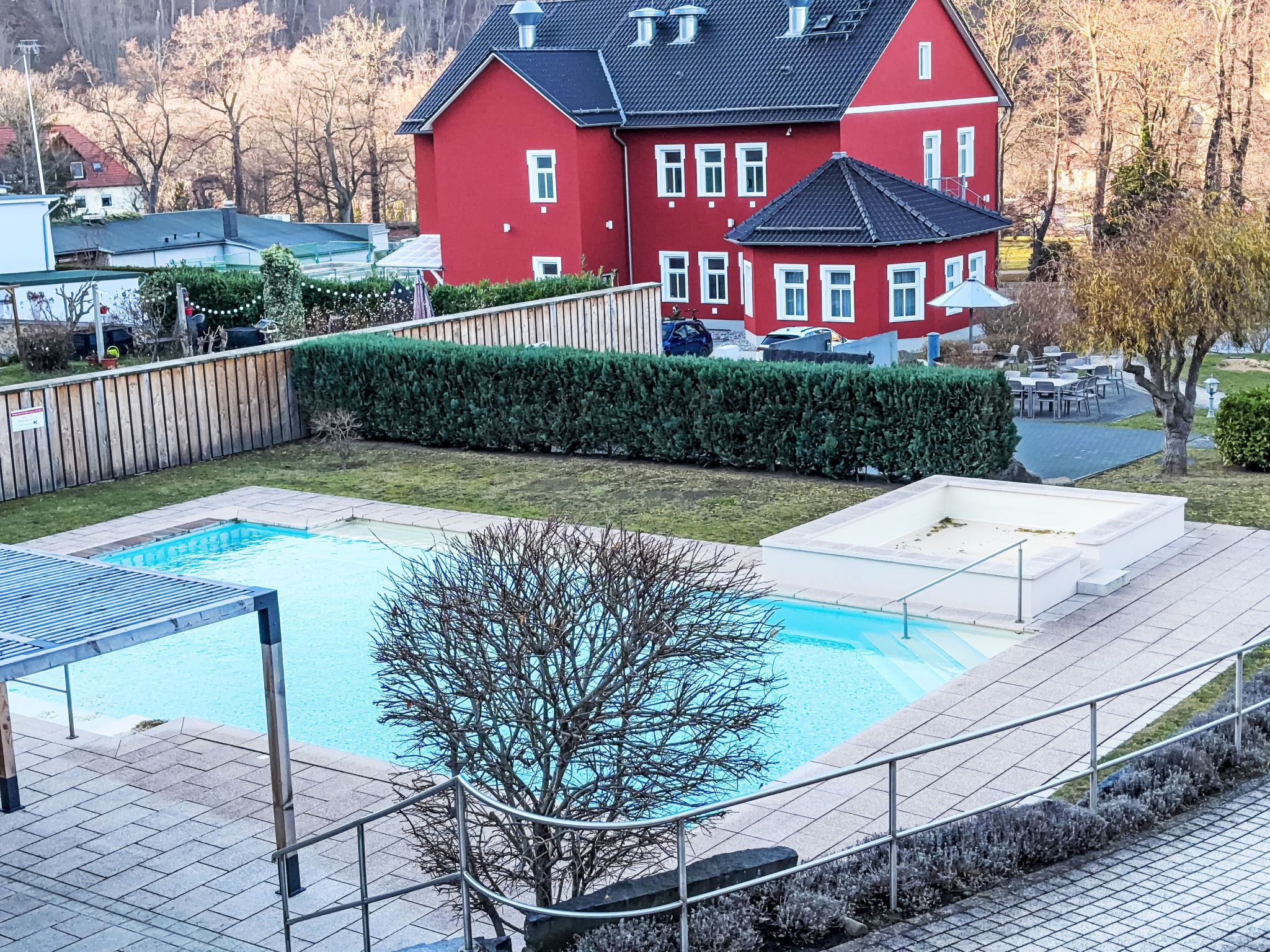 Una casa rossa con piscina, recinzione in legno e giardino curato.