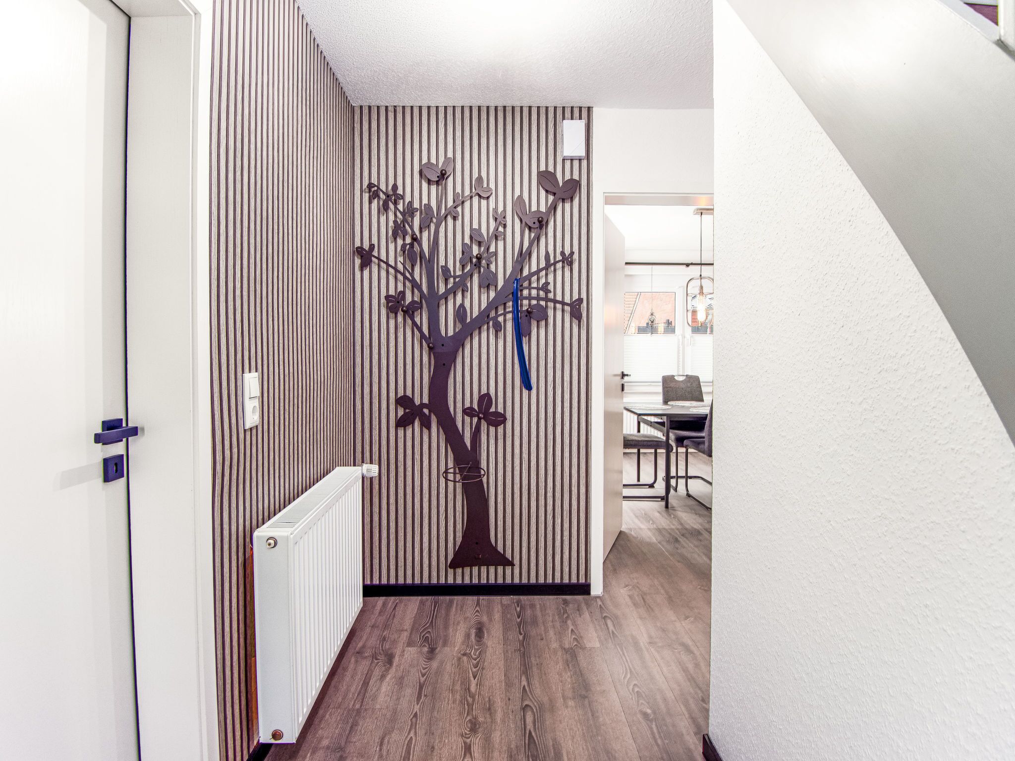 Un couloir avec un mur à rayures, un radiateur et, au fond, un coin repas.
