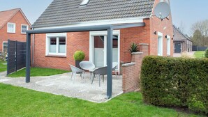 Een huis met een schuin dak, een schotelantenne en een overdekt terras met buitenmeubels.