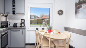 Een moderne keuken met inbouwapparatuur, een eethoek met houten stoelen, en een raam met uitzicht op huizen.