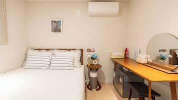 A bedroom with a bed, bedside table, lamp, and a small trash bin.