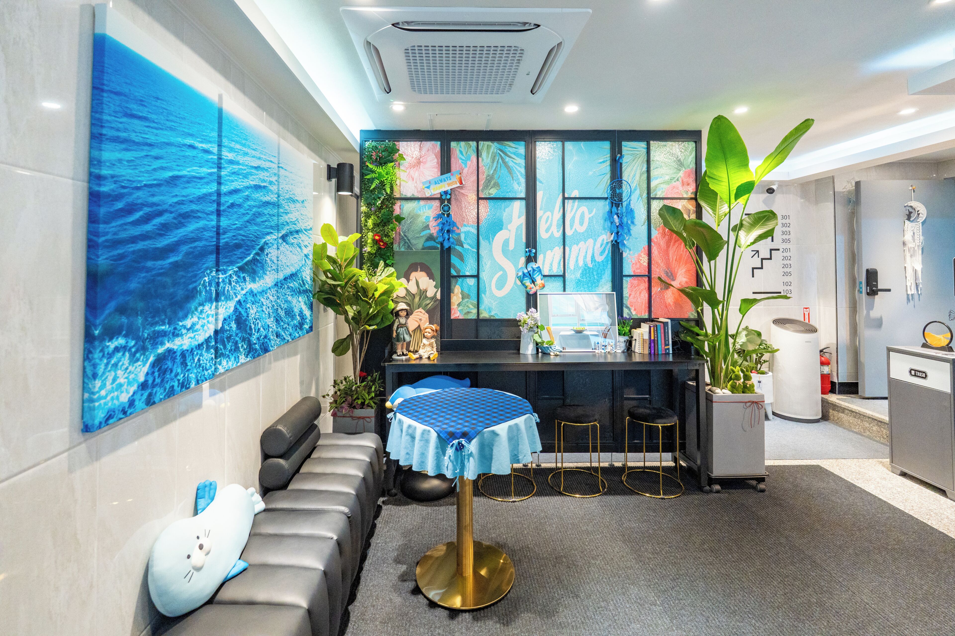 A modern hotel lobby with a blue ocean mural, a reception desk, a seating area, and a large plant.